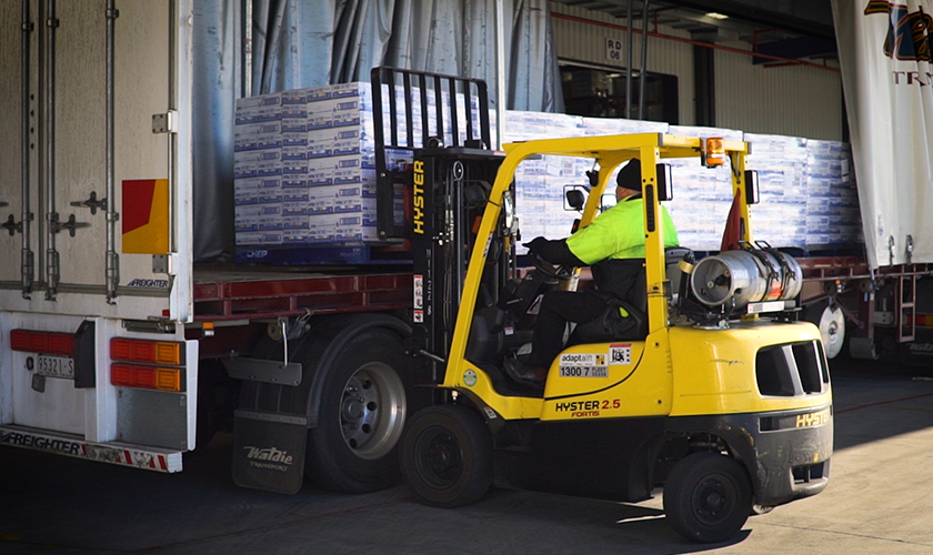 Forklift with worker in yellow vest loading goods into truck at warehouse.